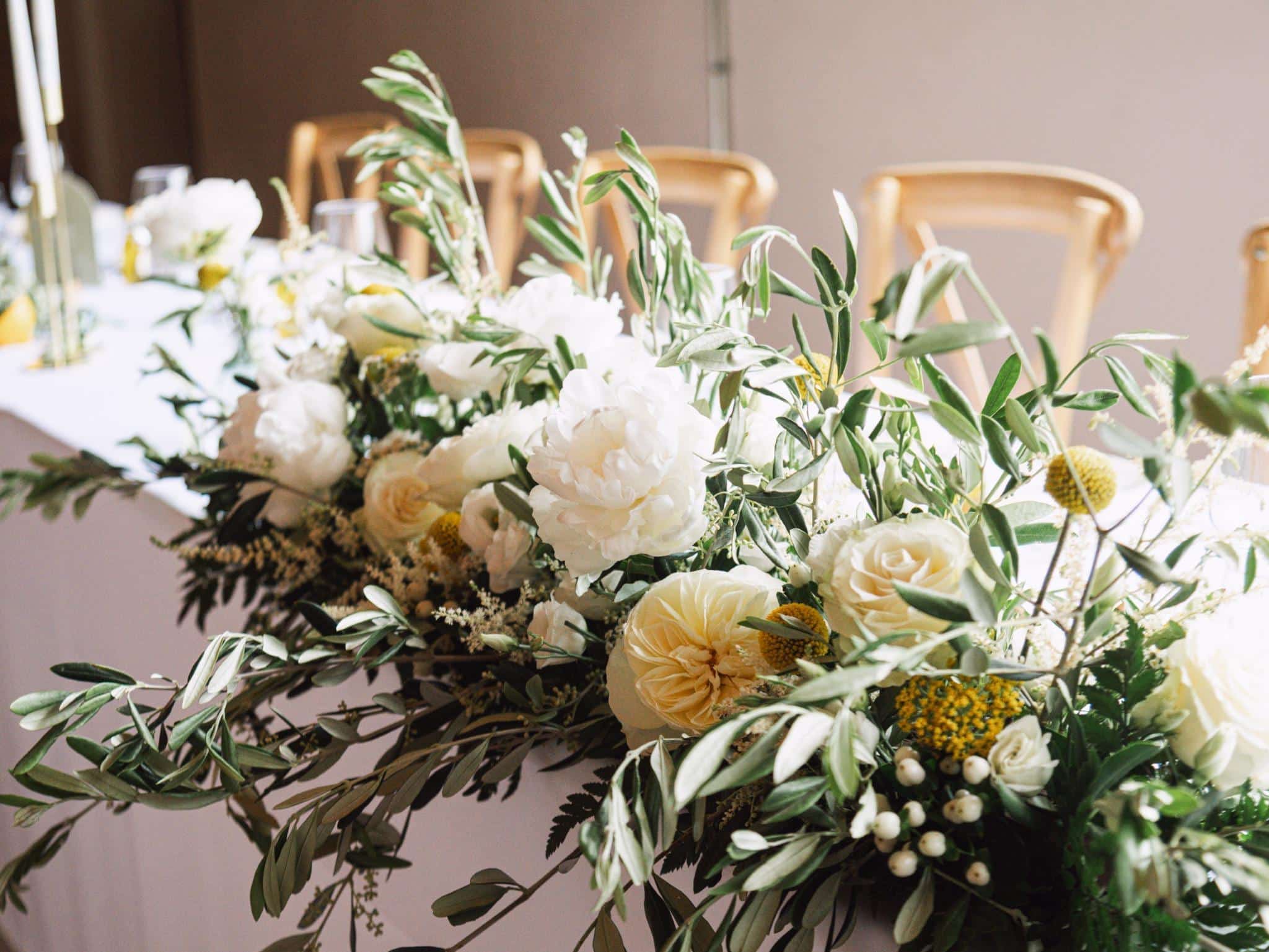 Centre de table de mariage composé de roses blanches, de fleurs jaunes et de feuillage.