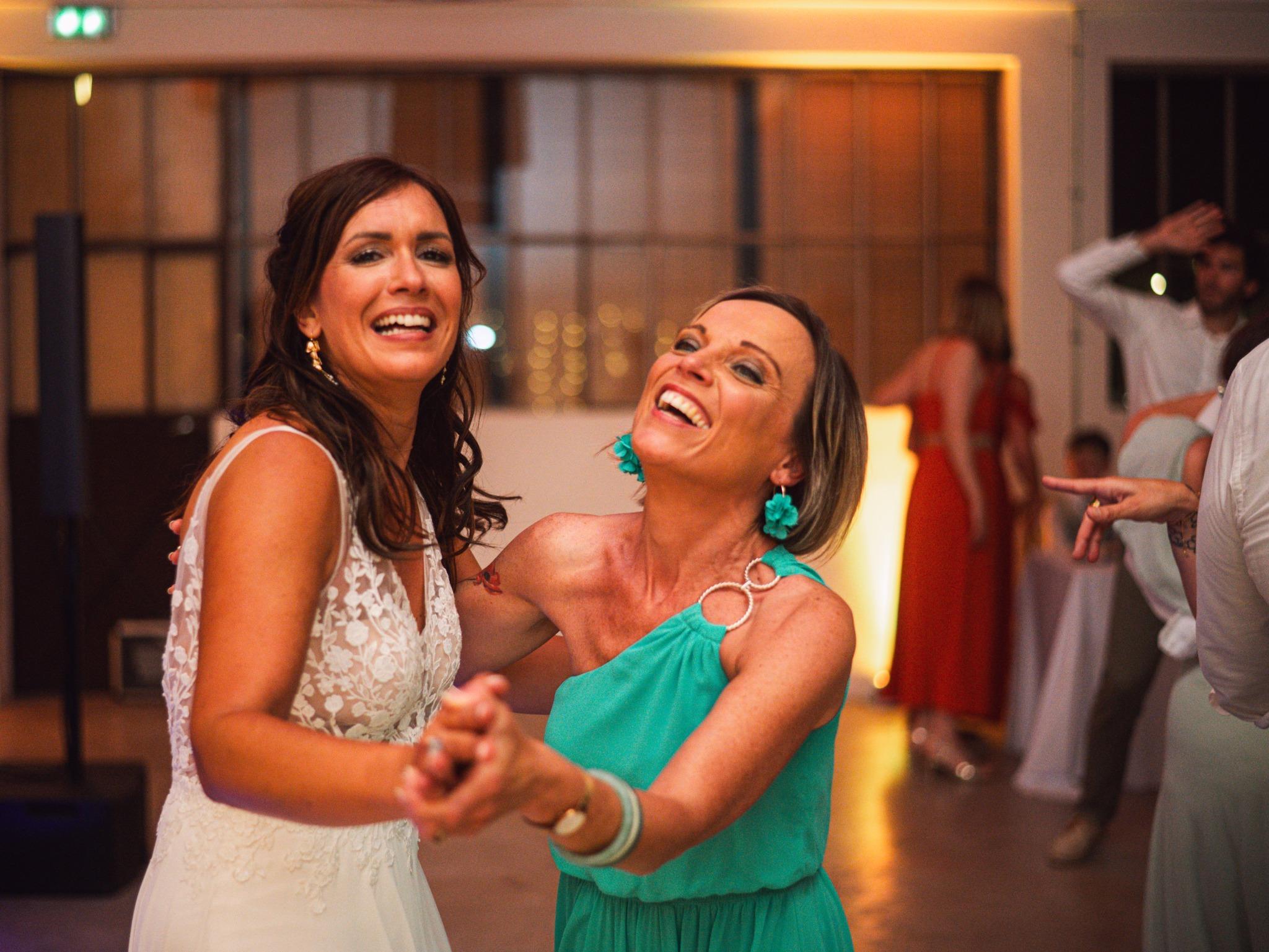 La mariée et une invitée en robe turquoise dansent en riant pendant la soirée du mariage.