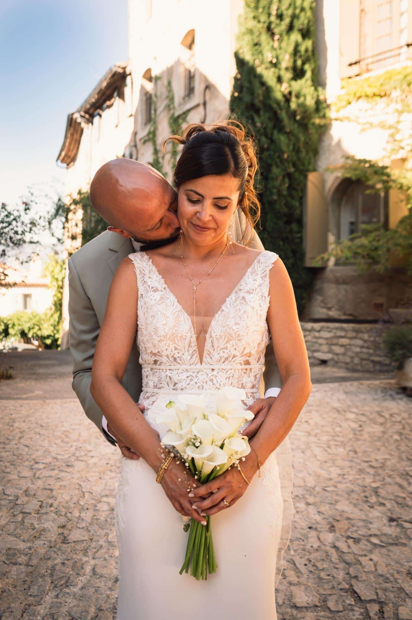 Le marié embrasse tendrement la mariée qui tient un bouquet de fleurs blanches.