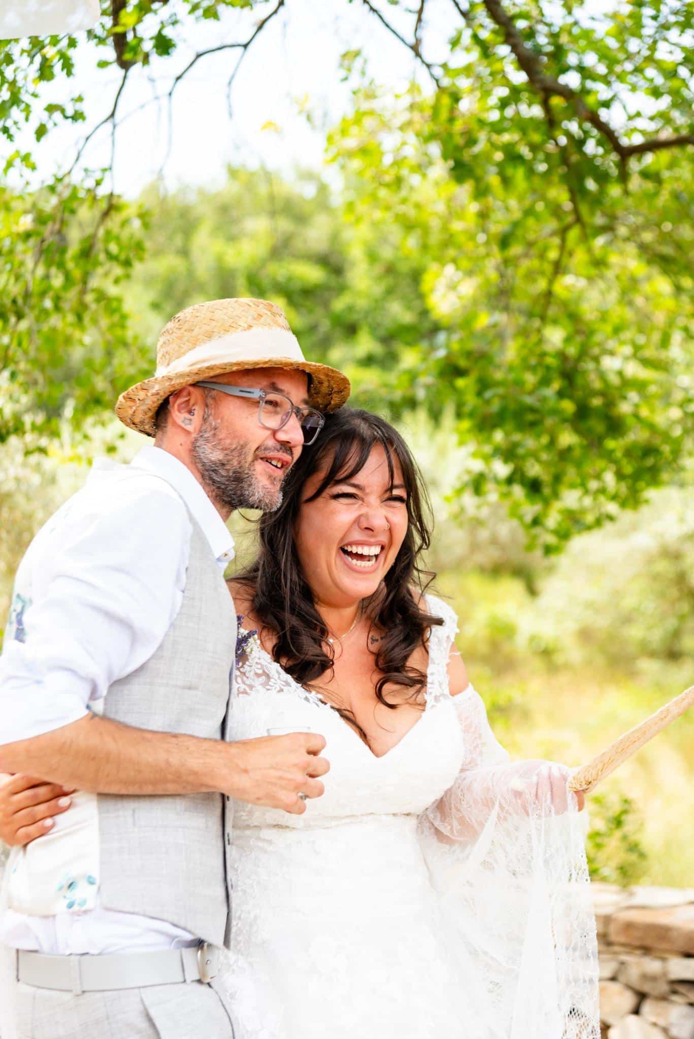 Un couple de mariés éclate de rire ensemble en plein air, dans un instant spontané.