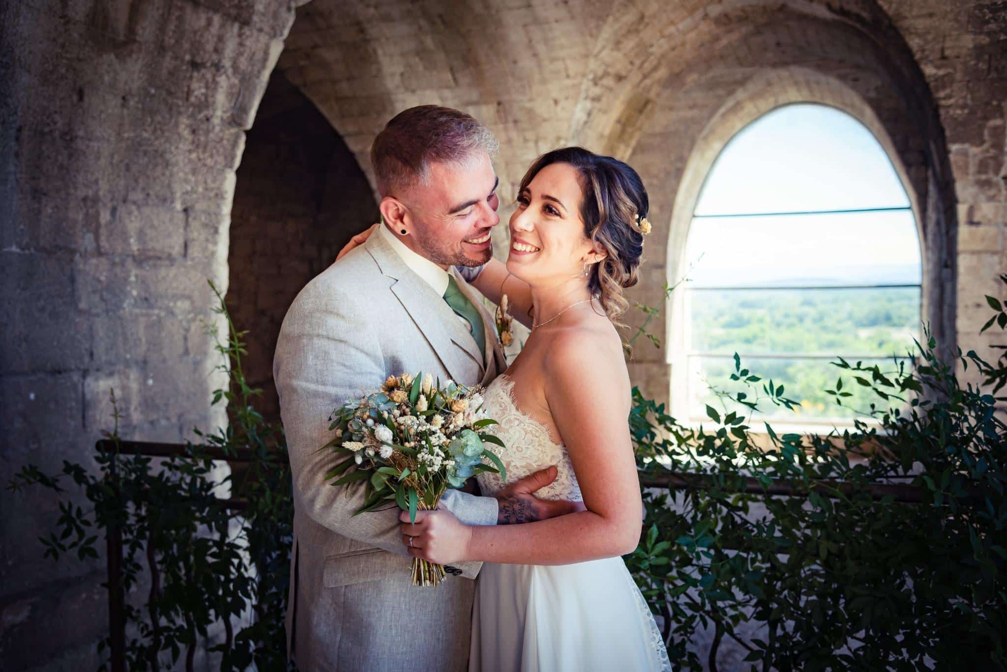 Un couple de mariés échange un regard complice sous une voûte en pierre.